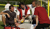 Foto: Ein DRK-Kursleiter erklärt den Kursteilnehmern auf einem Sportfeld die Benutzung einer Beatmungsmaske.